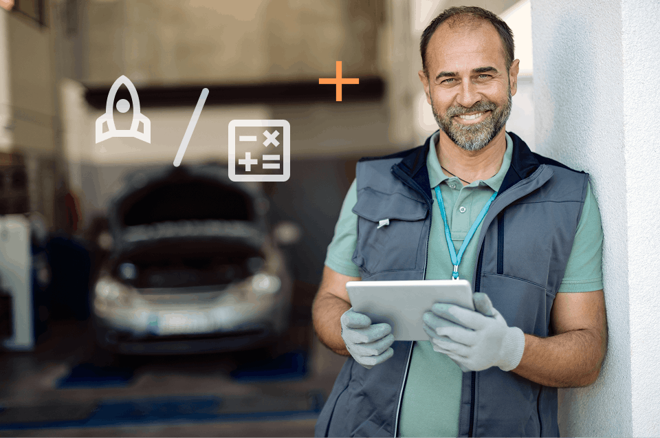 Smiling mechanic wearing gloves and a grey vest leaning against a white wall, holding a tablet, with a car in a garage in the background.